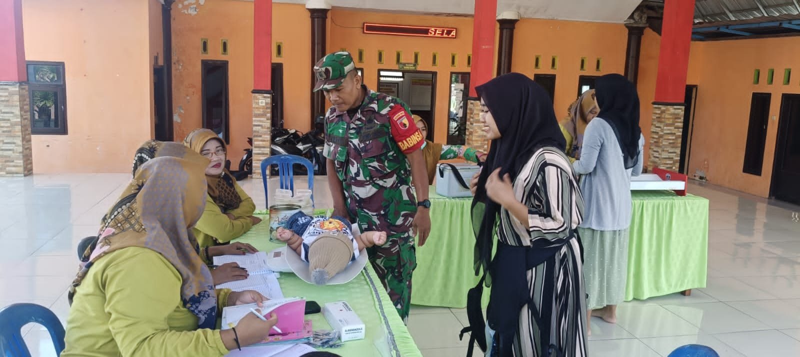 Babinsa Desa Sekarjoho Bantu Kegiatan Posyandu di Balai Desa Sekarjoho, Kecamatan Prigen, Kabupaten Pasuruan