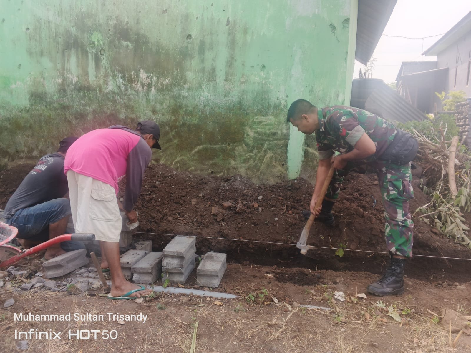 Babinsa Koramil Kuripan Koptu Sainal, bersama warga Dusun Krajan, Desa Jatisari, Kecamatan Kuripan, bergotong royong membangun pagar di Madrasah Darul Ulum.